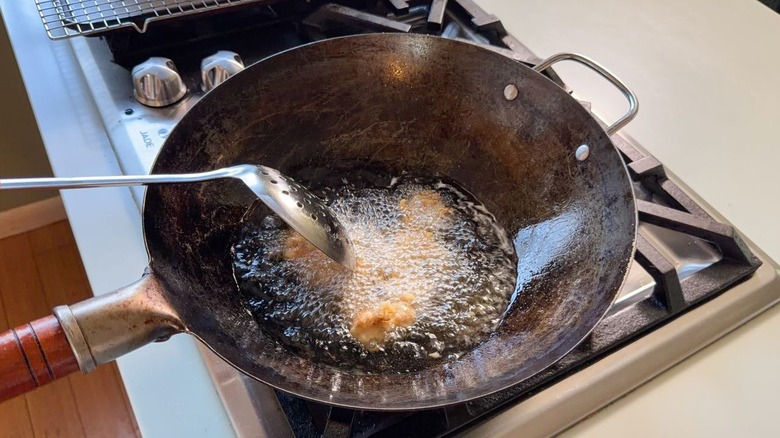 Frying sesame chicken pieces in hot peanut oil in wok on stovetop