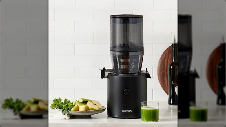 Hurom H-320 Slow Juicer with fruits and a glass of green juice on the side