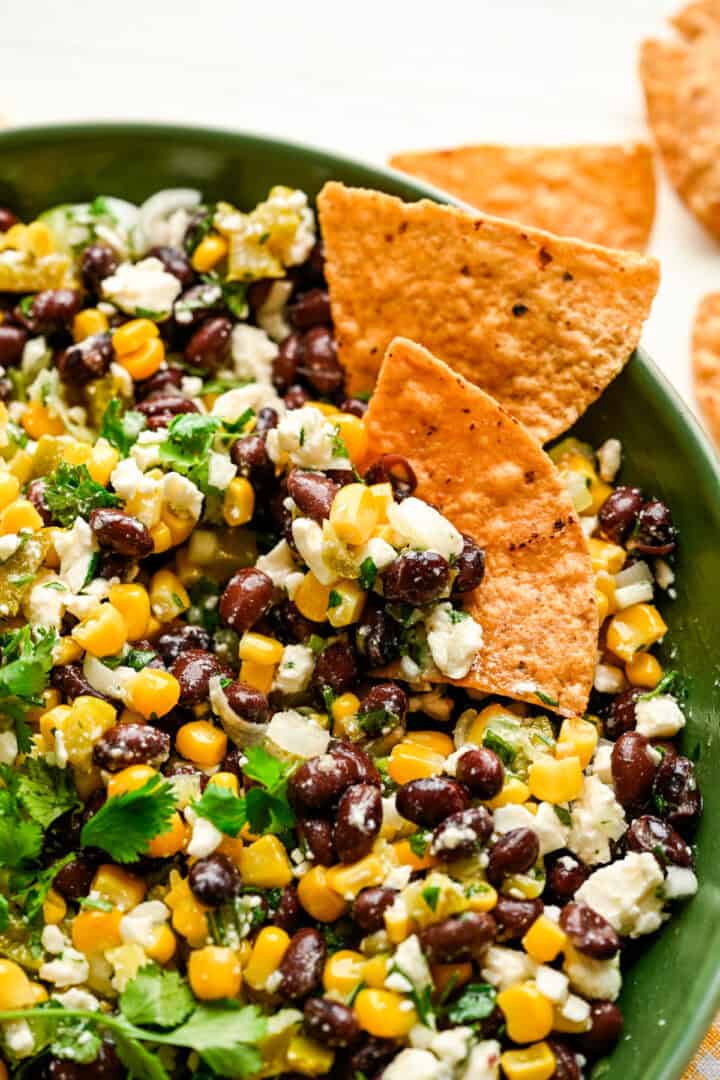 Close up view of black bean corn feta dip in a green bowl with tortilla chips on the side.