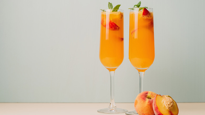 Two bellini cocktails in champagne flutes with peach and mint garnish