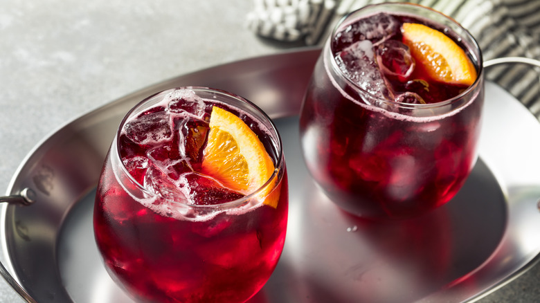 Two red wine spritzers in stemless wine glasses on a silver tray garnished with orange wedges