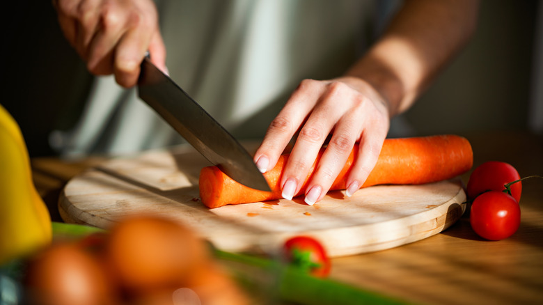 A person's hands are seen cutting a carrot.