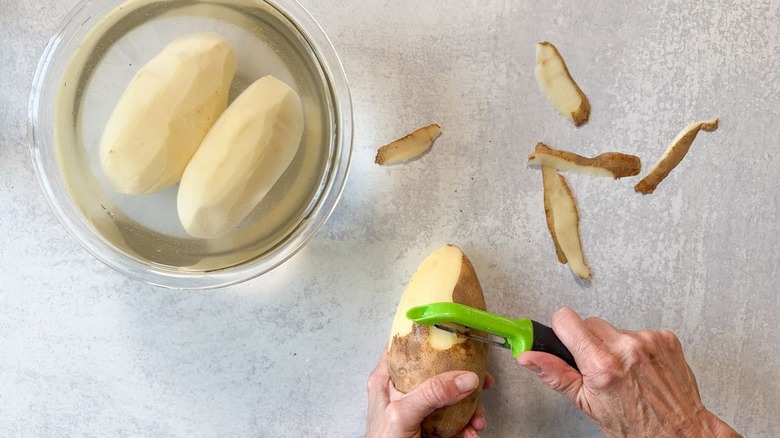 Peeling potatoes next to glass bowl filled with water and peeled potatoes