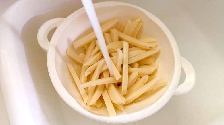 Rinsing potato batons in colander under cold water