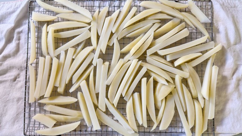 Par-cooked peeled potato batons on rack over kitchen towels