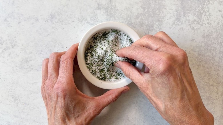 Mixing together salt and fresh dill in small bowl using fingertips