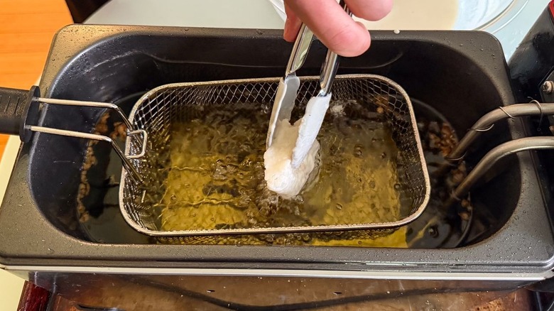 Lowering battered cod filet into fryer oil with tongs