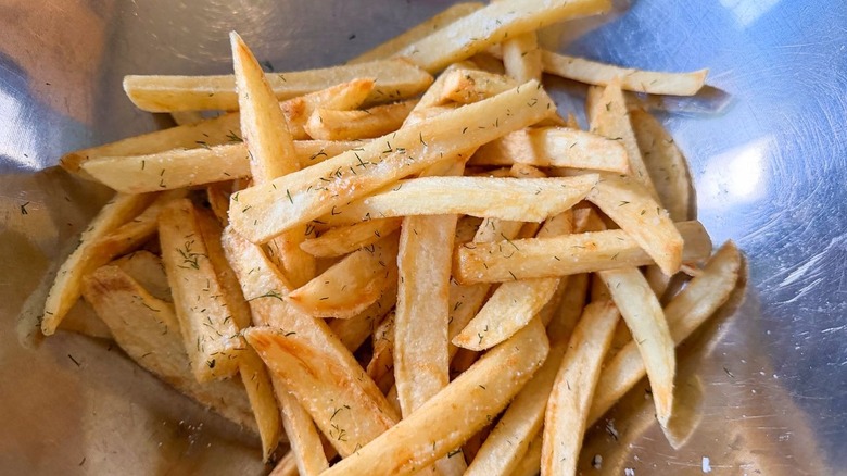 Tossing freshly fried chips with dill salt in stainless steel bowl