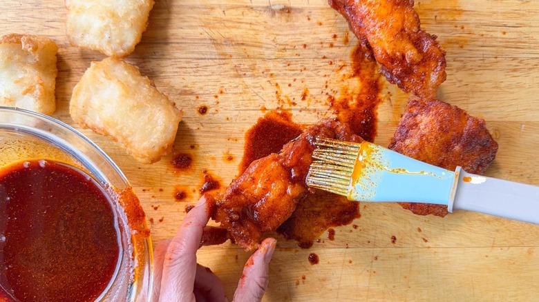 Using a pastry brush to apply Nashville hot glaze to fried cod filets on cutting board