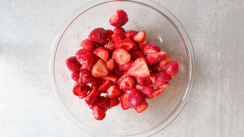 Fresh strawberry halves marinating in orange sugar in glass bowl