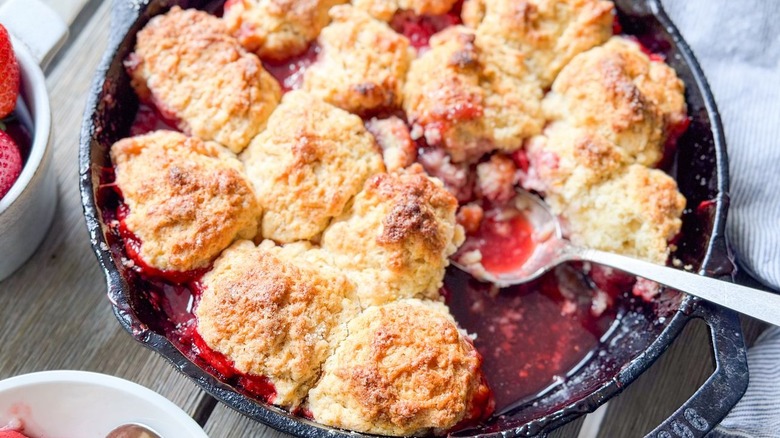 Strawberry and cardamom biscuit cobbler in cast iron skillet with piece scooped out
