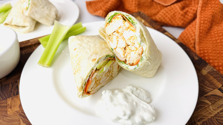 Buffalo chicken wrap halved on plate with celery and blue cheese dressing