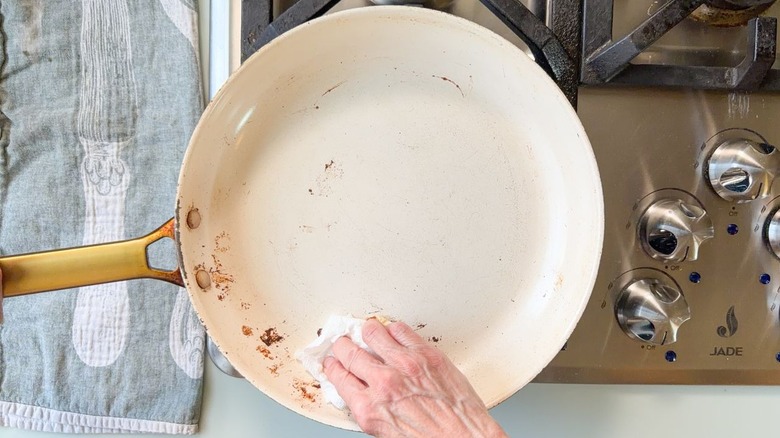 Wiping down a white skillet on stovetop with paper towel