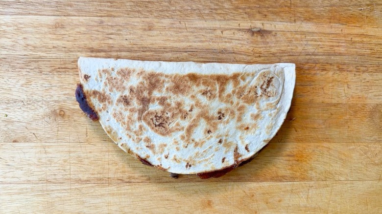 Cooked gooey cheesesteak quesadilla on cutting board