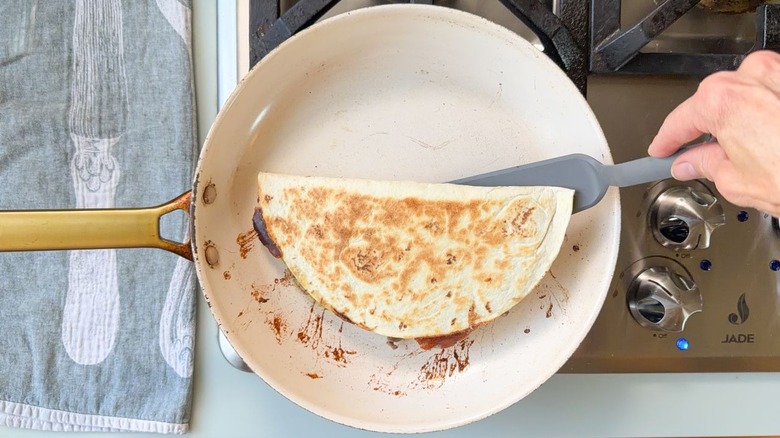 Flipping a gooey cheesesteak quesadilla in a skillet on stovetop
