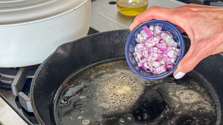 hand adding onions to pan