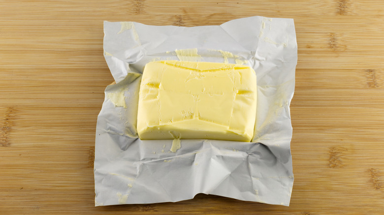 An unwrapped stick of butter on a wooden counter.
