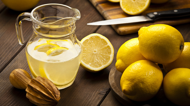 Small pitcher of lemonade with bowl of lemons and a wooden reamer