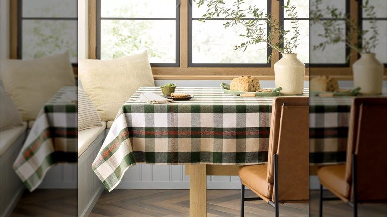 A plaid tablecloth with toffee brown and green colors dressing up a wood table with a chair behind it.