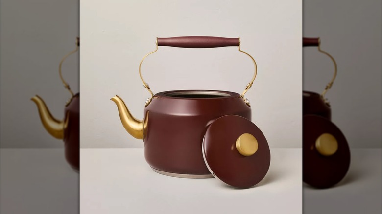 A dark red teapot with gold accents from Target sitting on a surface with its lid off.