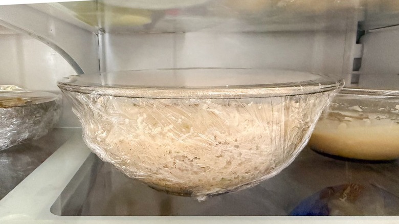 Crab cake egg roll filling chilling in plastic-covered glass bowl in refrigerator