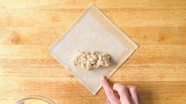 Adding egg wash to the edges of an egg roll wrapper on cutting board