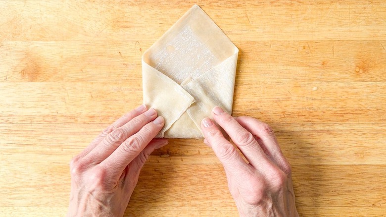 Folding a crab cake egg roll on a cutting board