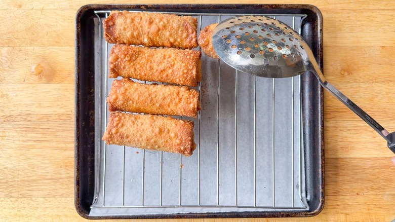 Transferring fried crab cake egg rolls to rack over parchment-lined sheet pan with slotted spoon