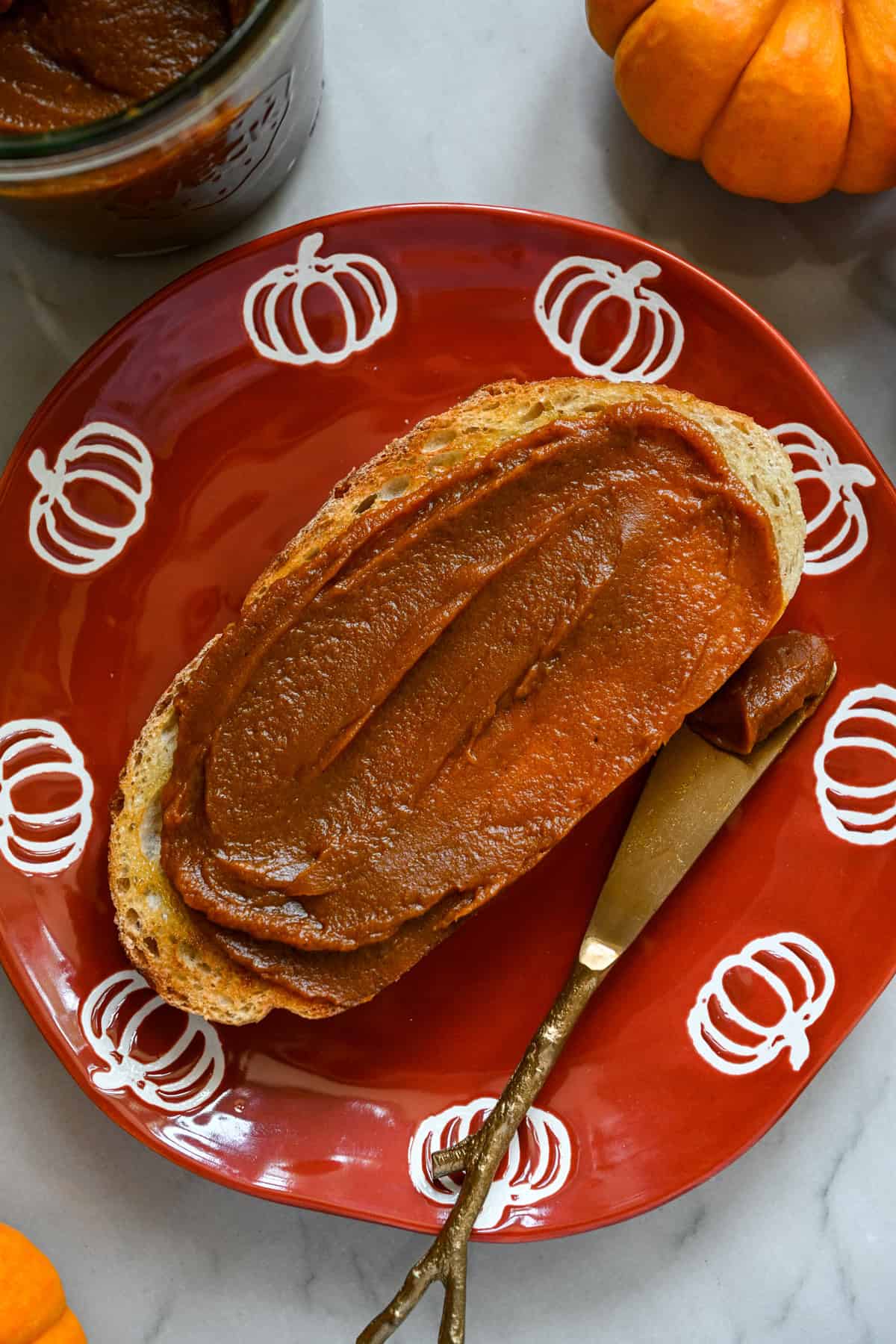 A slice of toast slathered with homemade pumpkin butter on an orange plate with pumpkins around the edge.