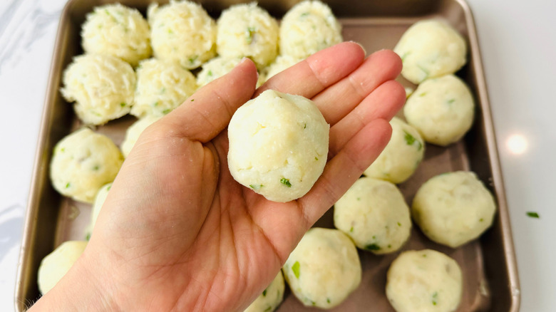 Hand holding mashed potato ball over sheet with mashed potato balls