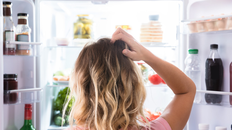 Person scratching their head while looking into an open refrigerator