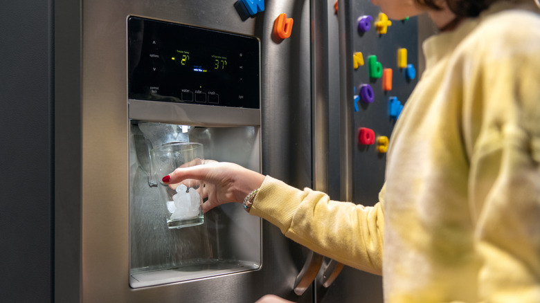 Person holding a glass under an automatic ice maker in a refrigerator door