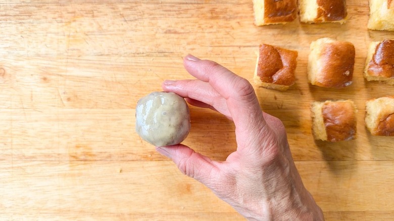 Placing a cheese-covered beef patty on a toasted brioche cube on cutting board