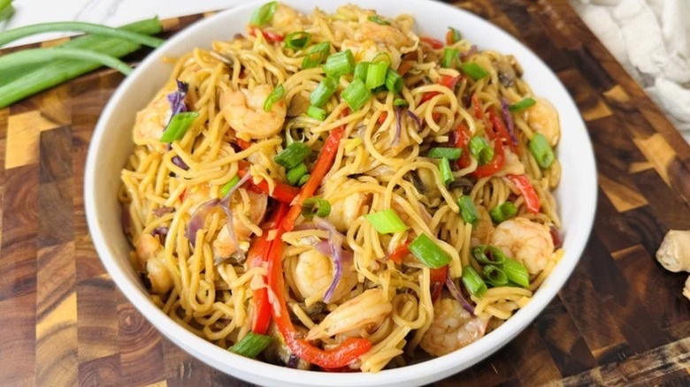 shrimp lo mein in a white bowl with noodles, protein, coleslaw, and chives visible
