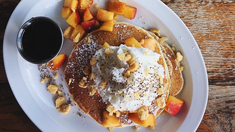 A plate of pancake with fruit, whipped cream, and syrup at Ria's Bluebird