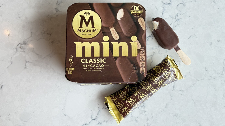 A Magnum Mini Classic Ice Cream Bar with a bite taken out of it sits next to its package