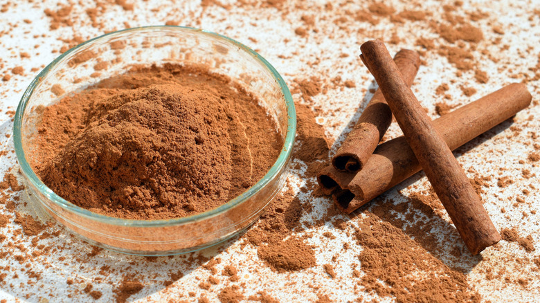 ground cinnamon in a glass bowl near cinnamon sticks.