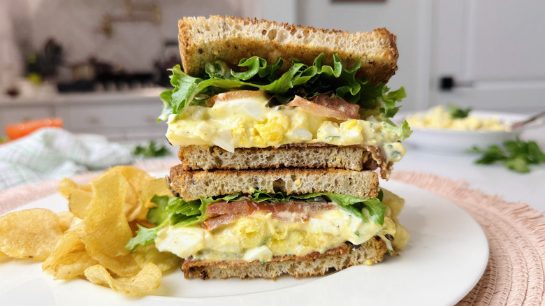 Egg salad club sandwich on plate with chips