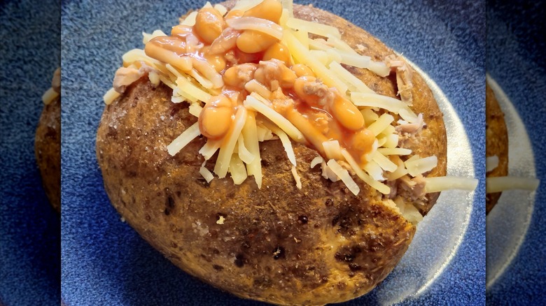 An excellent and hearty, typically English dish. These are jacket potatoes, whole potatoes baked in the oven with the peel and then stuffed. In the photo, the potato is cut in half and topped with tuna, beans, and thinly sliced ​​cheddar cheese.