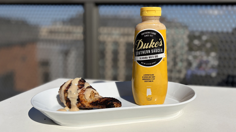 A bottle of Duke's Alabama White BBQ Sauce next to a chicken leg drizzled with the sauce