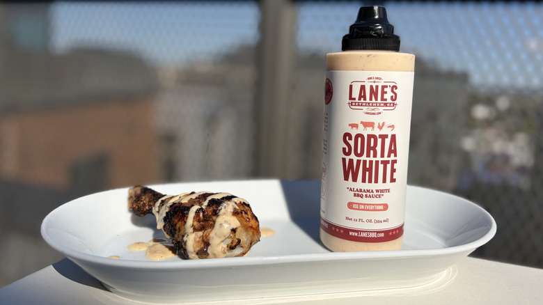 A bottle of Lane's Sorta White BBQ Sauce next to a chicken leg drizzled with the sauce