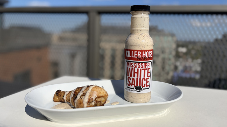 A bottle of Killer Hogs Mississippi White Sauce next to a chicken leg drizzled with the sauce