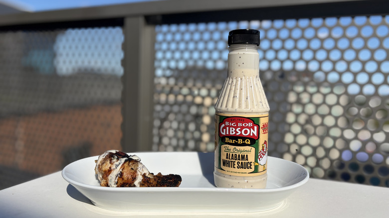 A bottle of Big Bob Gibson Original White Sauce next to a chicken leg drizzled with the sauce