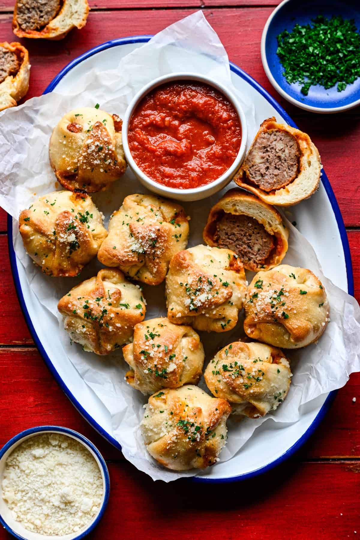 Overhead view af kødbolle-sub bidder på et piftet udstillingsfad med marinara, parmesan og persille ved siden af.