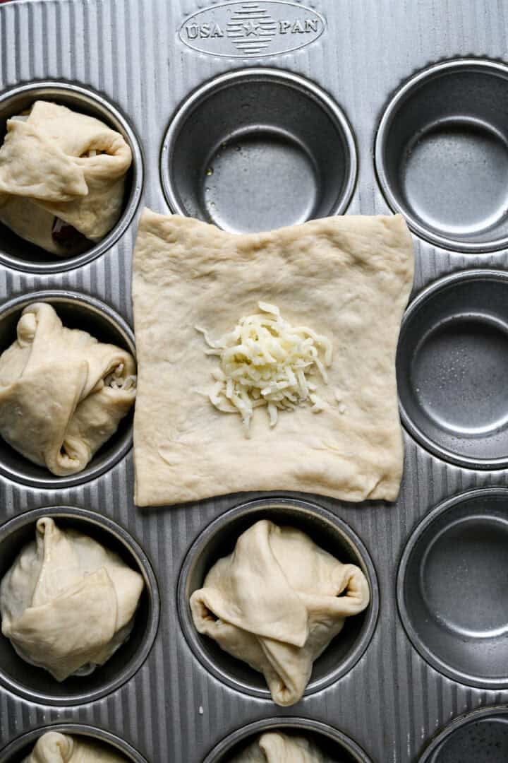 Overhead view af revet mozzarella toppet på et dejstykke i en smurt muffinsform.