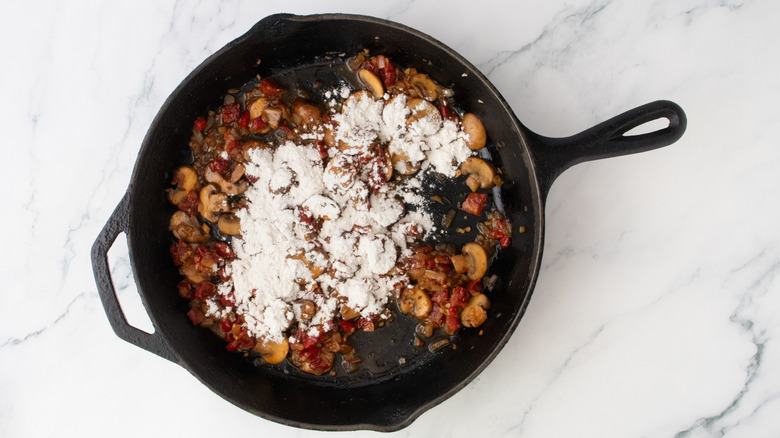Sauteed vegetables in a large skillet sprinkled with flour