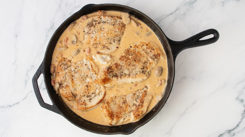 Seared chicken nestled into a cream sauce in a large skillet