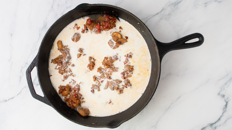A large skillet with vegetables, broth, and cream