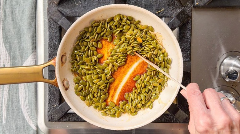 Stirring chile oil toasted pepitas in skillet with wooden spoon