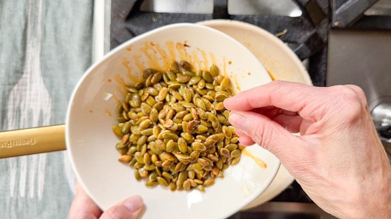 Sprinkling salt on chile oil-toasted pepitas in bowl